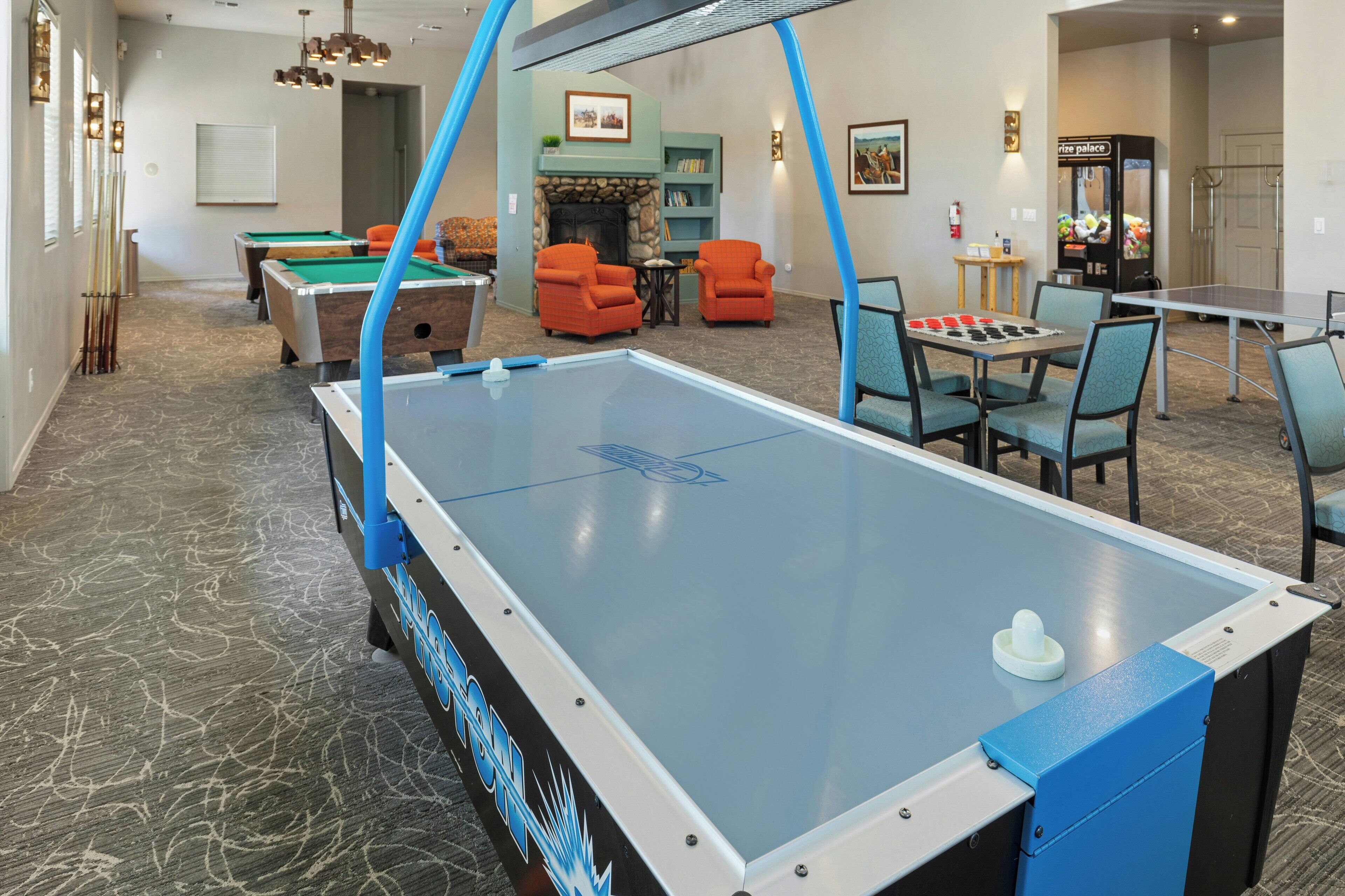 A pool table with surrounding seating, a billiards table, and a fireplace in a room with a carpeted floor.