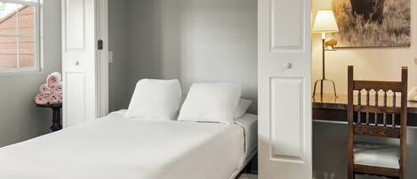 A bedroom with a bed, a chair, a desk, a lamp, and a wall-mounted picture.