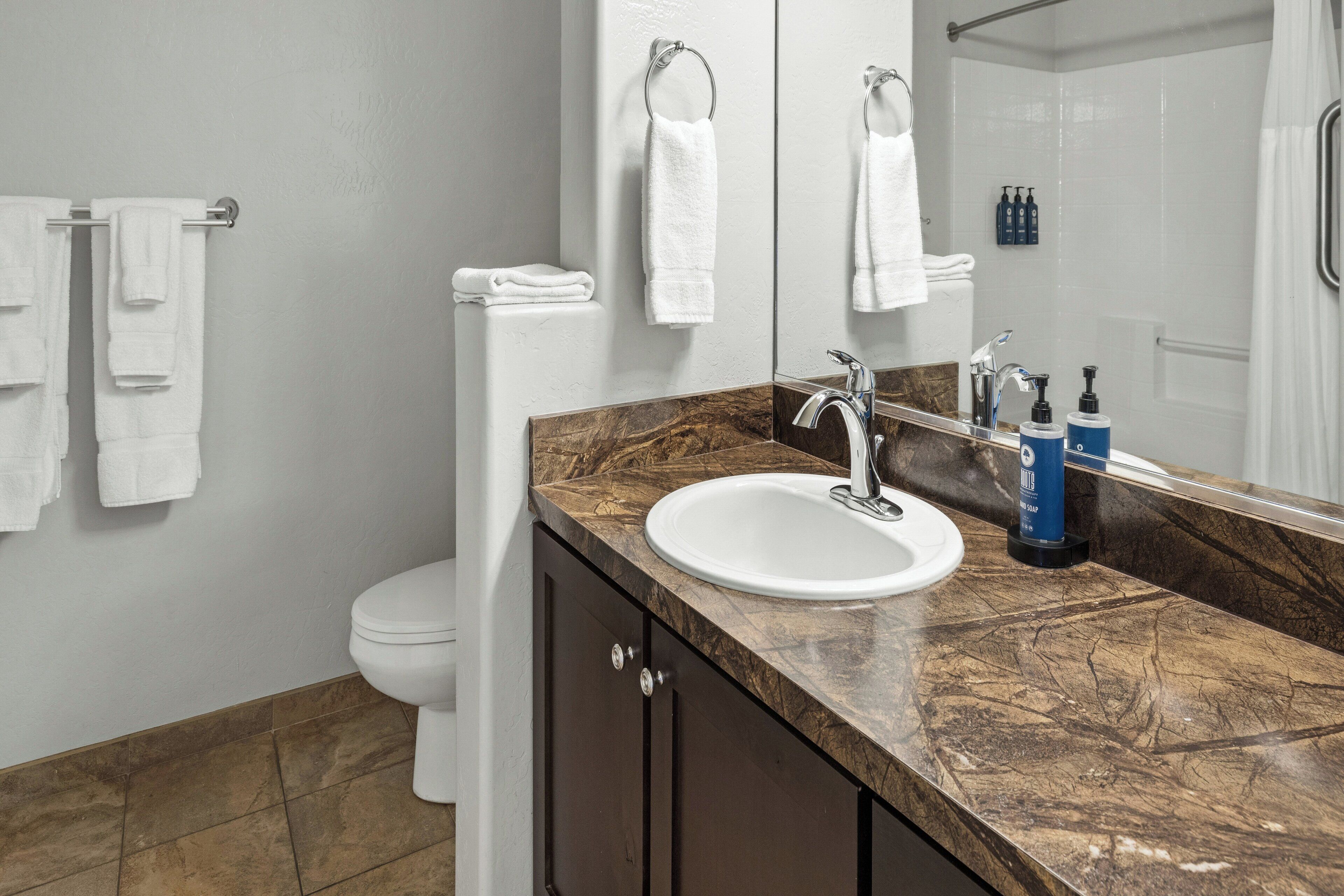 A bathroom with a marble countertop, a white sink, a mirror, and a toilet.