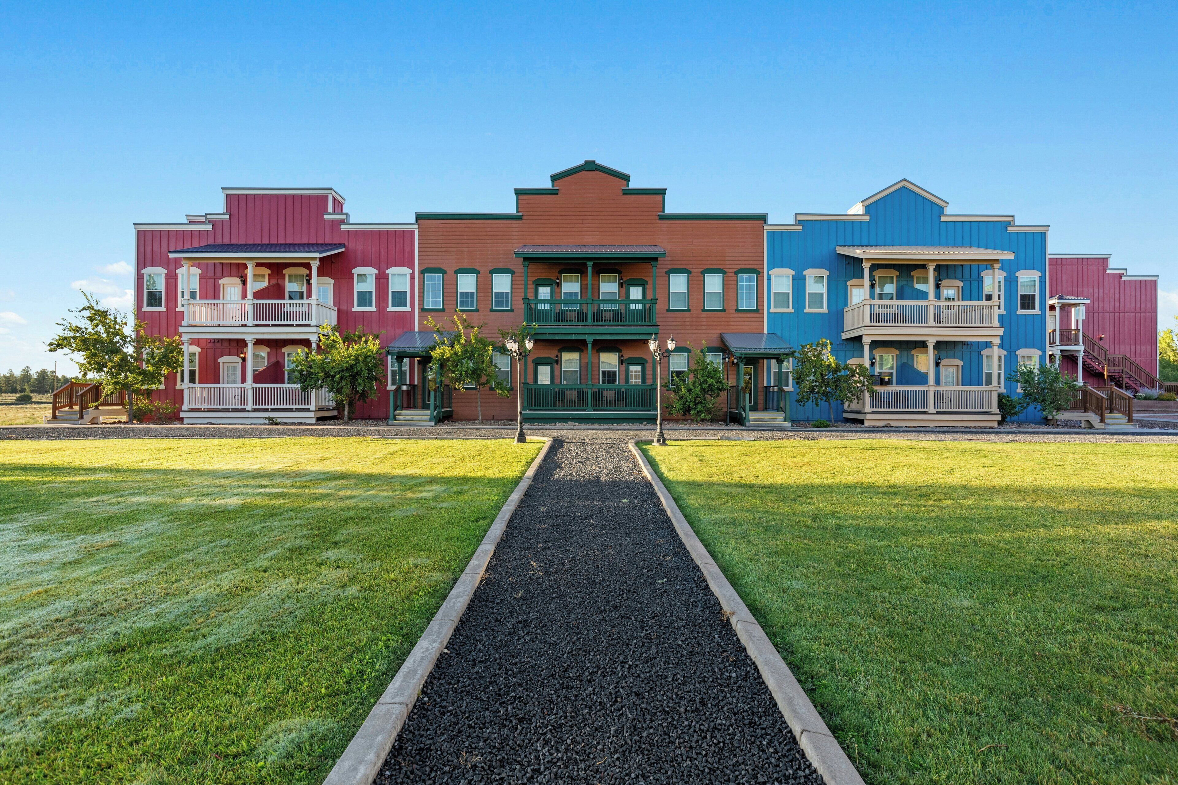 A row of colorful townhouses with a central entrance, a gravel pathway, and a well-maintained lawn.