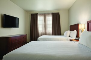 Habitación de hotel con dos camas, un televisor, una mesita de noche y una lámpara.