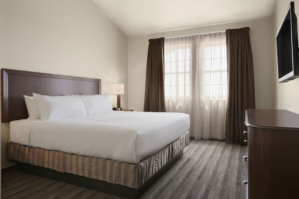 A hotel room with a large bed, a nightstand, a TV, and a dresser.