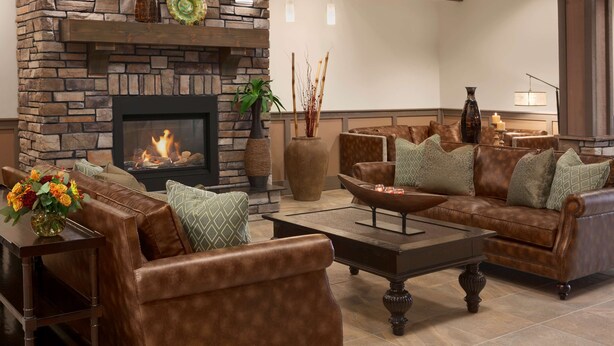 A cozy living room with a stone fireplace, leather sofas, and a coffee table. - HYATT house Minot (Minot)