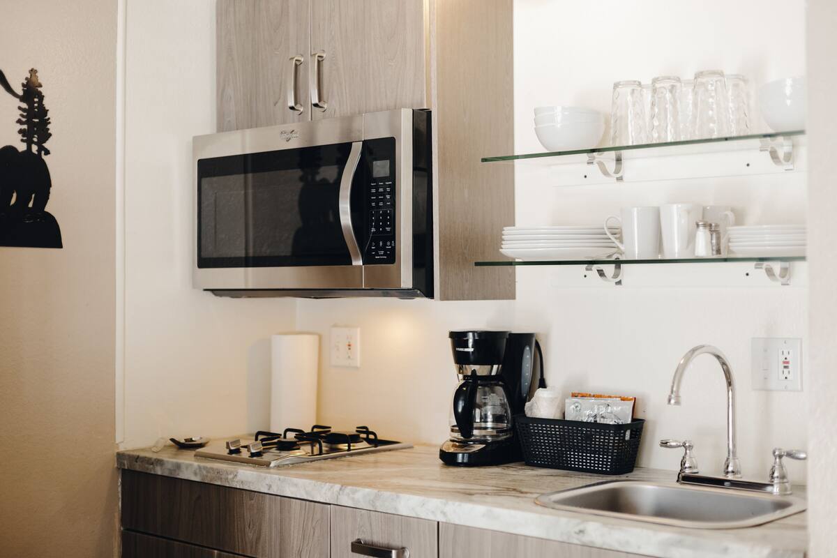 A modern kitchen with a built-in microwave, gas stove, coffee maker, and glass shelves above the sink.