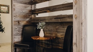 Un rincón con asientos, una pared de madera, dos sillones de cuero negro, una mesita con un florero y piso de baldosas.