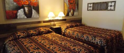 Camera d'albergo con due letti, ciascuno con una coperta a motivi decorativi, un comodino con una lampada e due quadri appesi al muro.
