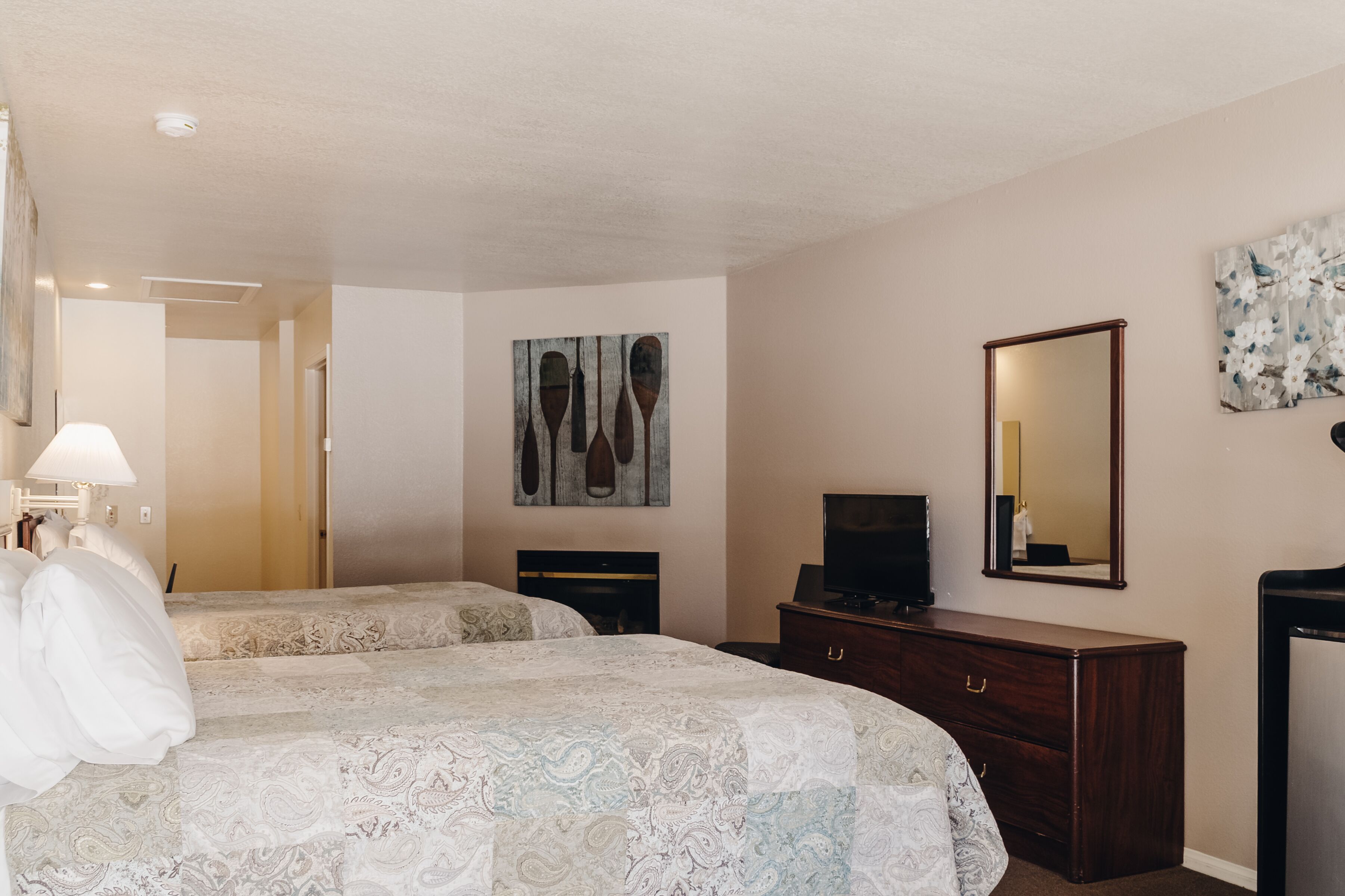 Une chambre d’hôtel avec deux lits, une commode, un téléviseur et des œuvres d’art accrochées aux murs.