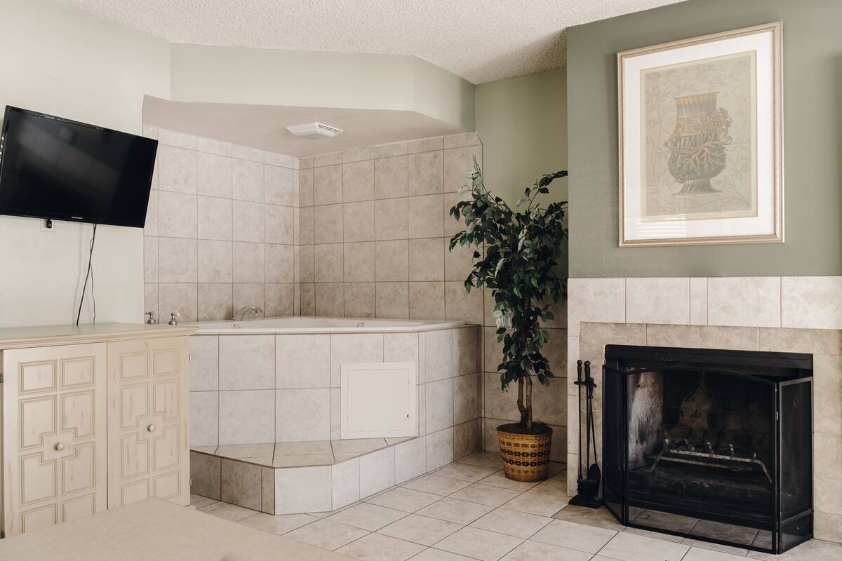A bathroom with a bathtub, a sink, a mirror, a television, and a framed picture on the wall.