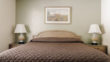 Ein ordentlich bezogenes Bett mit einem gemusterten Bettbezug, zwei Nachttischlampen und einem gerahmten Bild an der Wand.