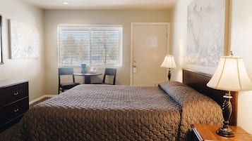 Quarto com cama, escrivaninha, duas cadeiras, janela com persianas e porta.