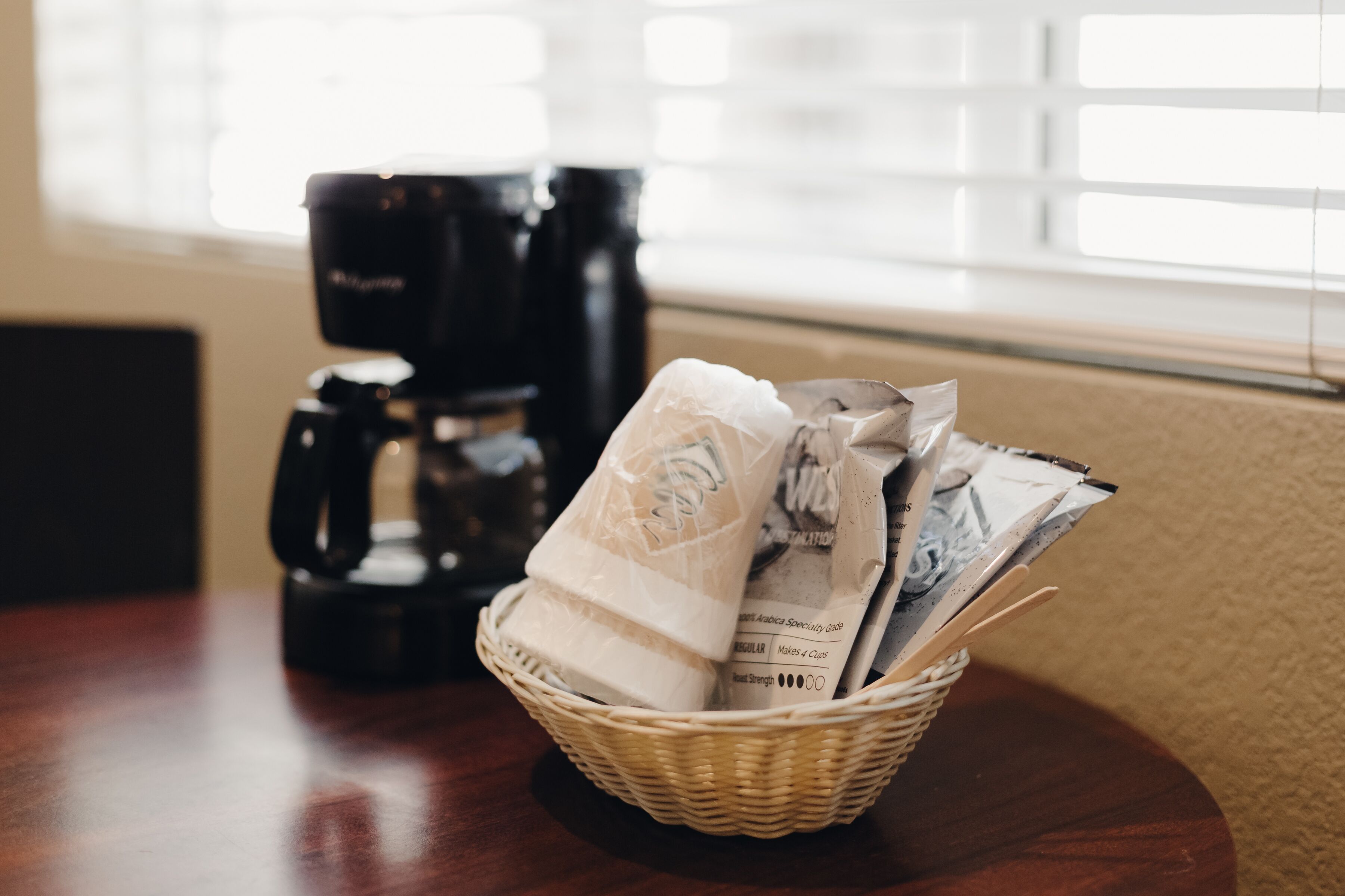 Een rieten mand op een tafel met koffiekapsules en een koffiezetapparaat op de achtergrond.