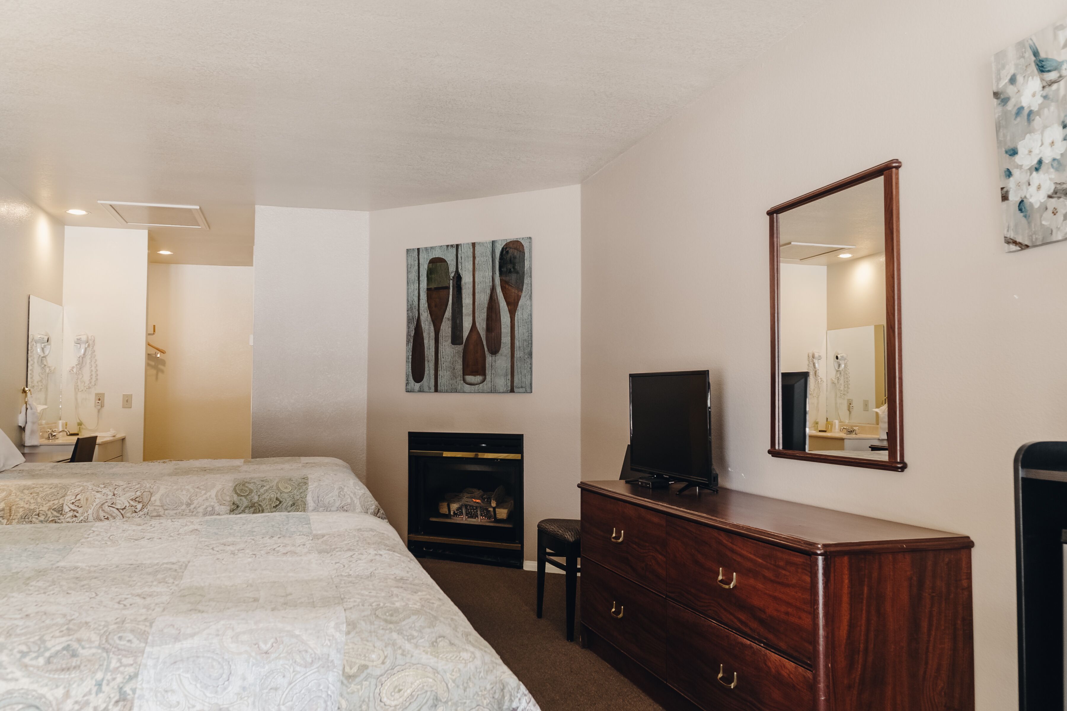 A bedroom with two beds, a dresser, a television, a fireplace, and artwork on the walls.