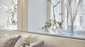 A seating area with a bench and cushions, a window with a view of buildings, and a vase with branches and flowers on the windowsill.