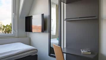 Una habitación de hotel moderna con una cama, un televisor montado en la pared, una silla y una estantería con un libro.