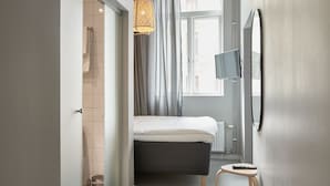 A modern hotel room with a bed, a TV, a small table, and a window with curtains.
