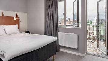 Una habitación de hotel moderna con una cama grande, una mesita de noche, una ventana con cortinas y vistas a la ciudad.
