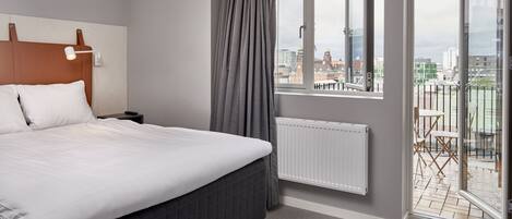 Una habitación de hotel moderna con una cama grande, una mesita de noche, una ventana con cortinas y vistas a la ciudad.