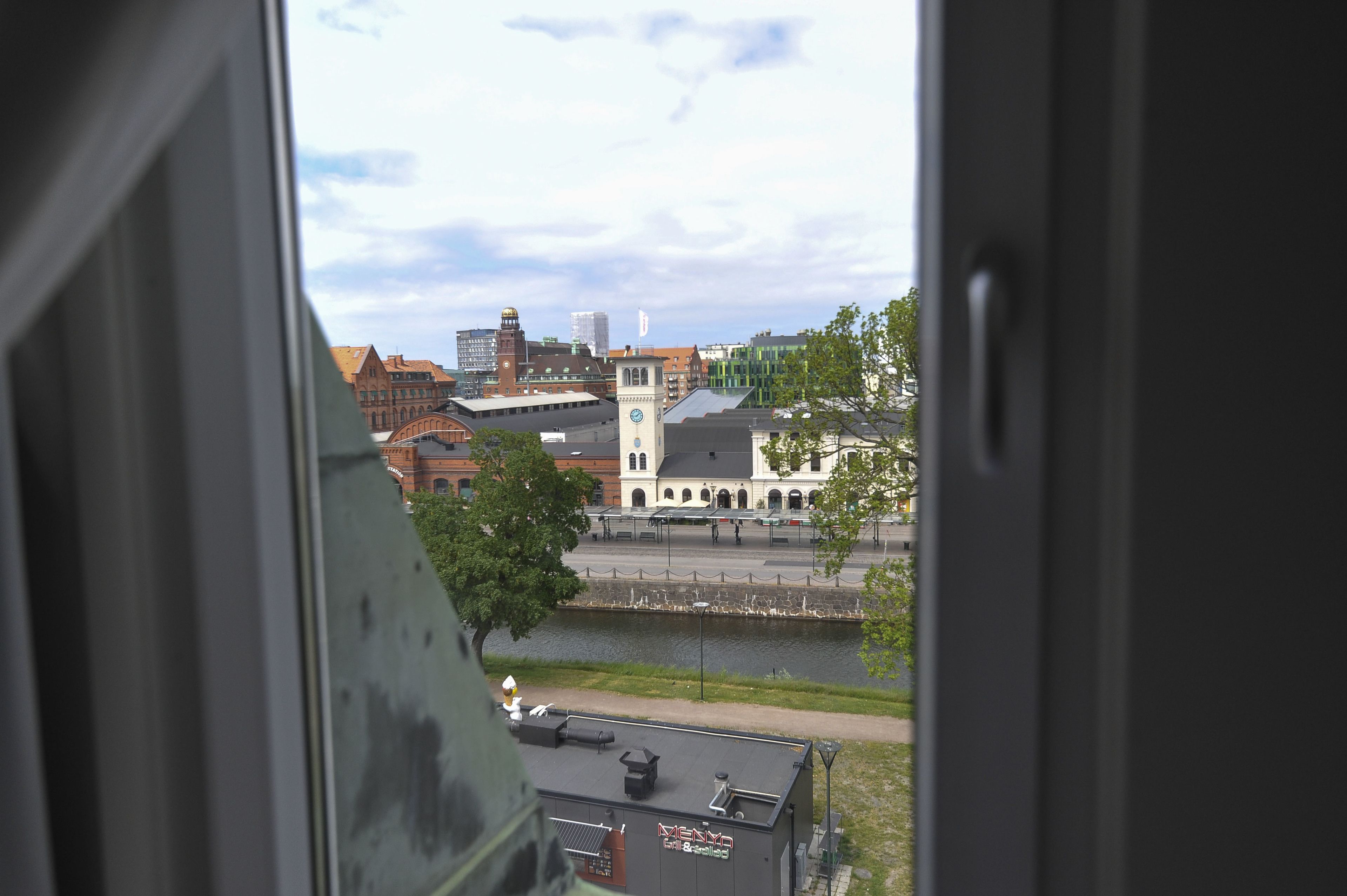 Uitzicht door een raam op een stadsgezicht met gebouwen, een rivier en een klokkentoren.