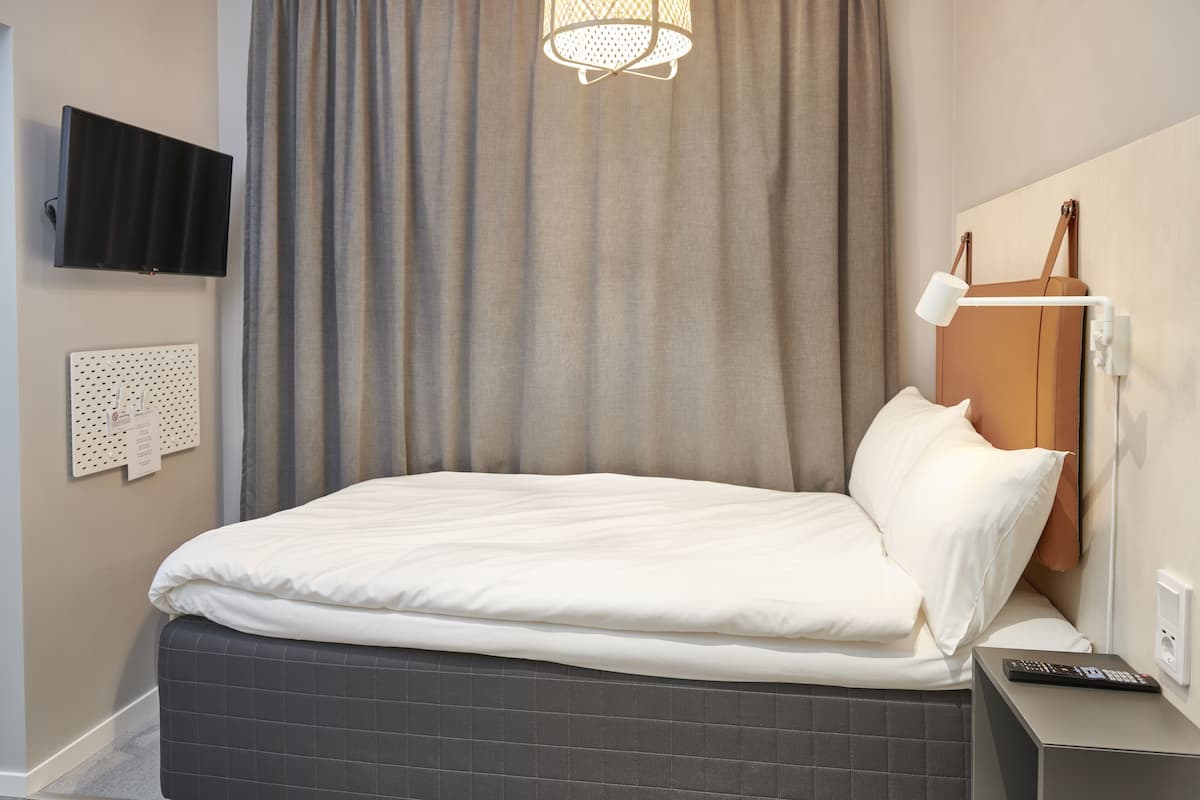 A neatly made bed with white linens, a bedside table with a lamp, and a flat-screen TV mounted on the wall.