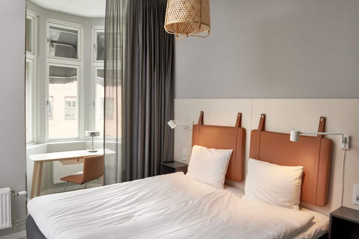 A neatly arranged hotel room with a large bed, a desk, and a window with curtains.