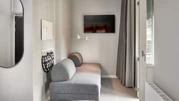 A modern bedroom with a grey sofa, a wall-mounted TV, a mirror, and a radiator.