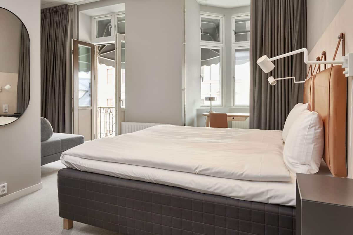Hotellihuone, jossa on sänky, työpöytä, tuoli, peili ja ikkuna, jossa on verhot.