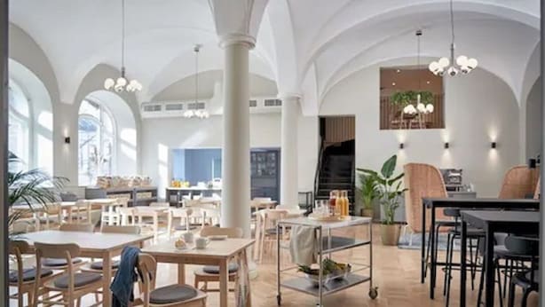 A spacious dining area with high ceilings, wooden tables and chairs, and pendant lighting.