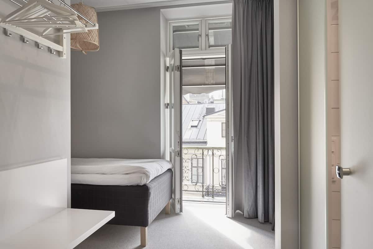 A bedroom with a bed, a drying rack, and a view of the outside balcony.