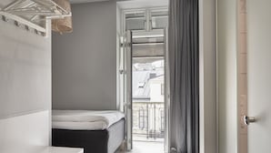 A bedroom with a bed, a drying rack, and a view of the outside balcony.