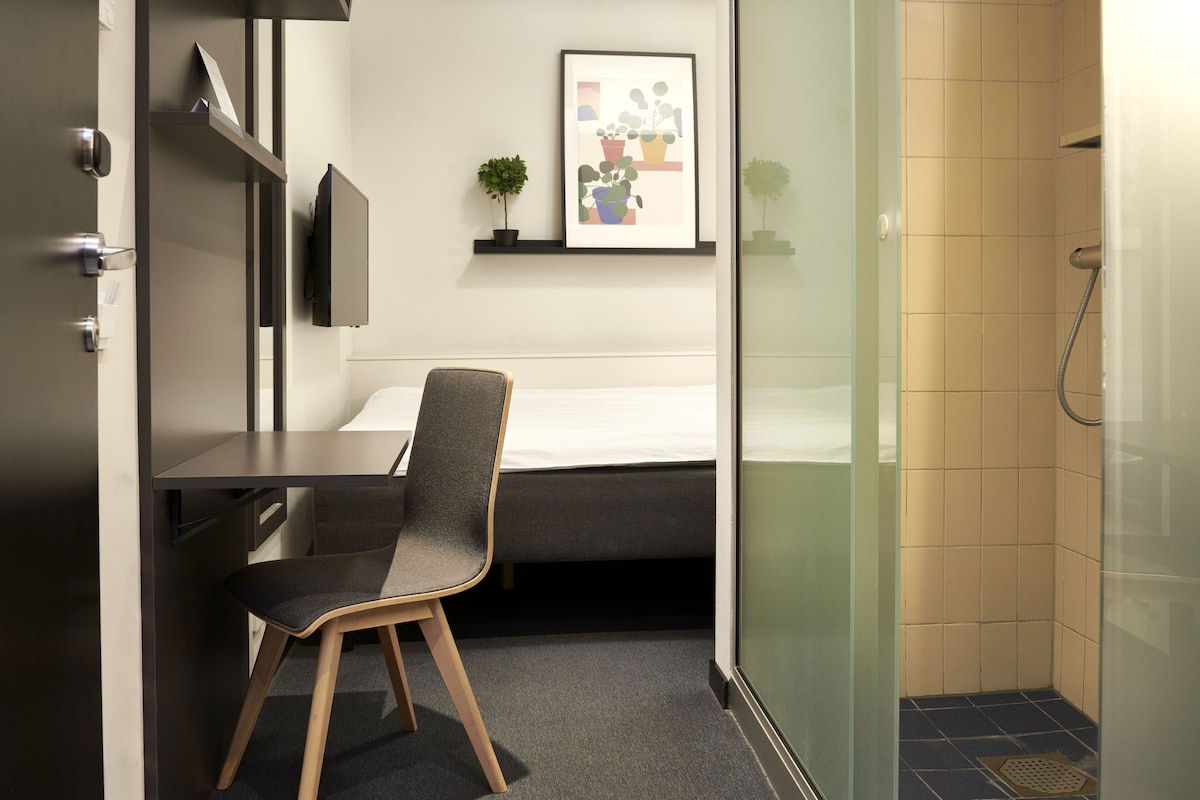A modern hotel room with a desk, chair, bed, and a shower area.