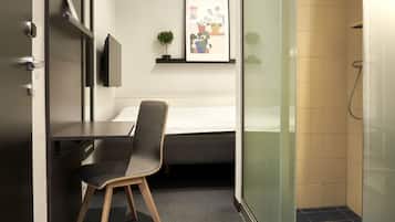 Quarto de hotel moderno com escrivaninha, cadeira, cama e área de chuveiro.