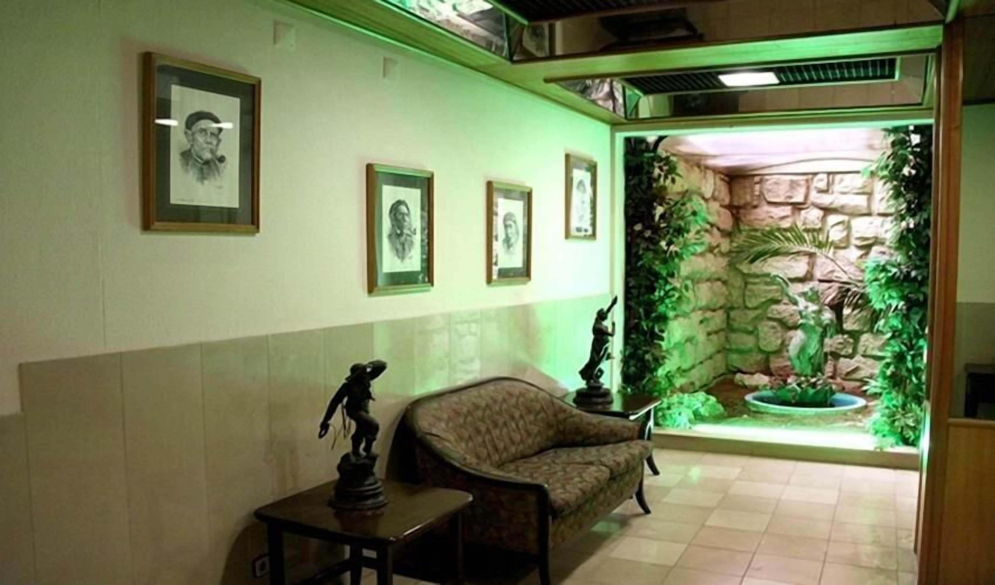 A reception area with framed portraits on the wall, a statue on a table, and a stone wall with plants.