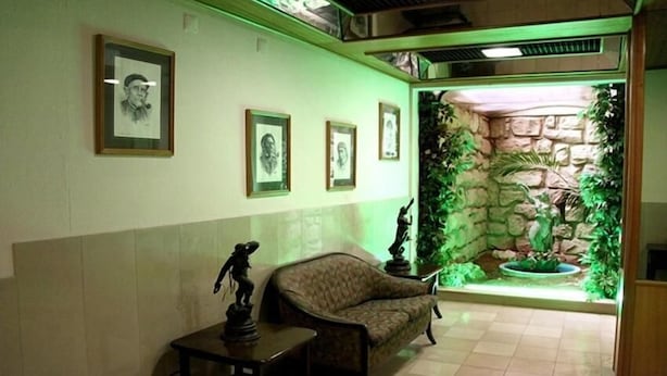 A reception area with framed portraits on the wall, a statue on a table, and a stone wall with plants.