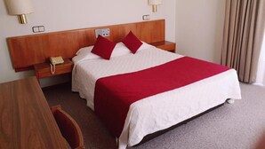A hotel room with a wooden headboard, two bedside tables with lamps, a telephone, a red and white bedspread, and a framed picture on the wall.
