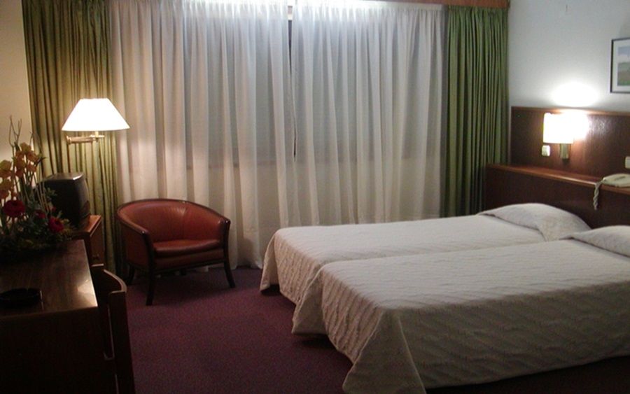 Una habitación de hotel con una cama, una silla, una lámpara y una mesita de noche.