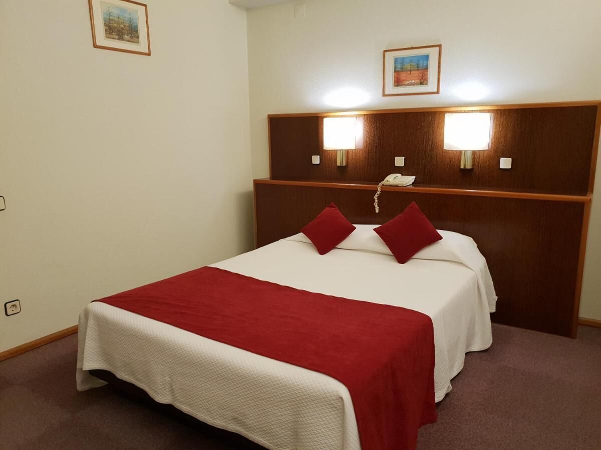 Habitación de hotel con una cama, dos lámparas de noche y dos cuadros en la pared.
