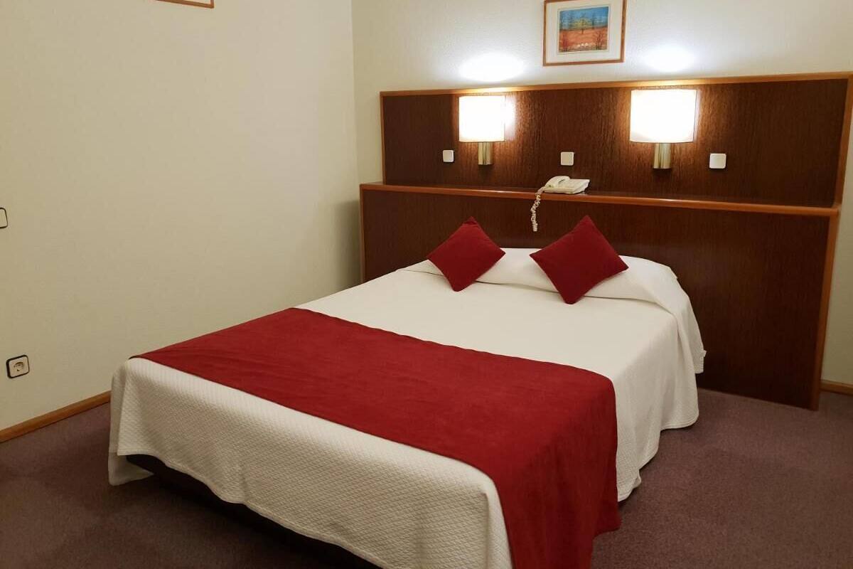 Una habitación de hotel con una cama, dos lámparas de noche y un cabecero con una lámpara.