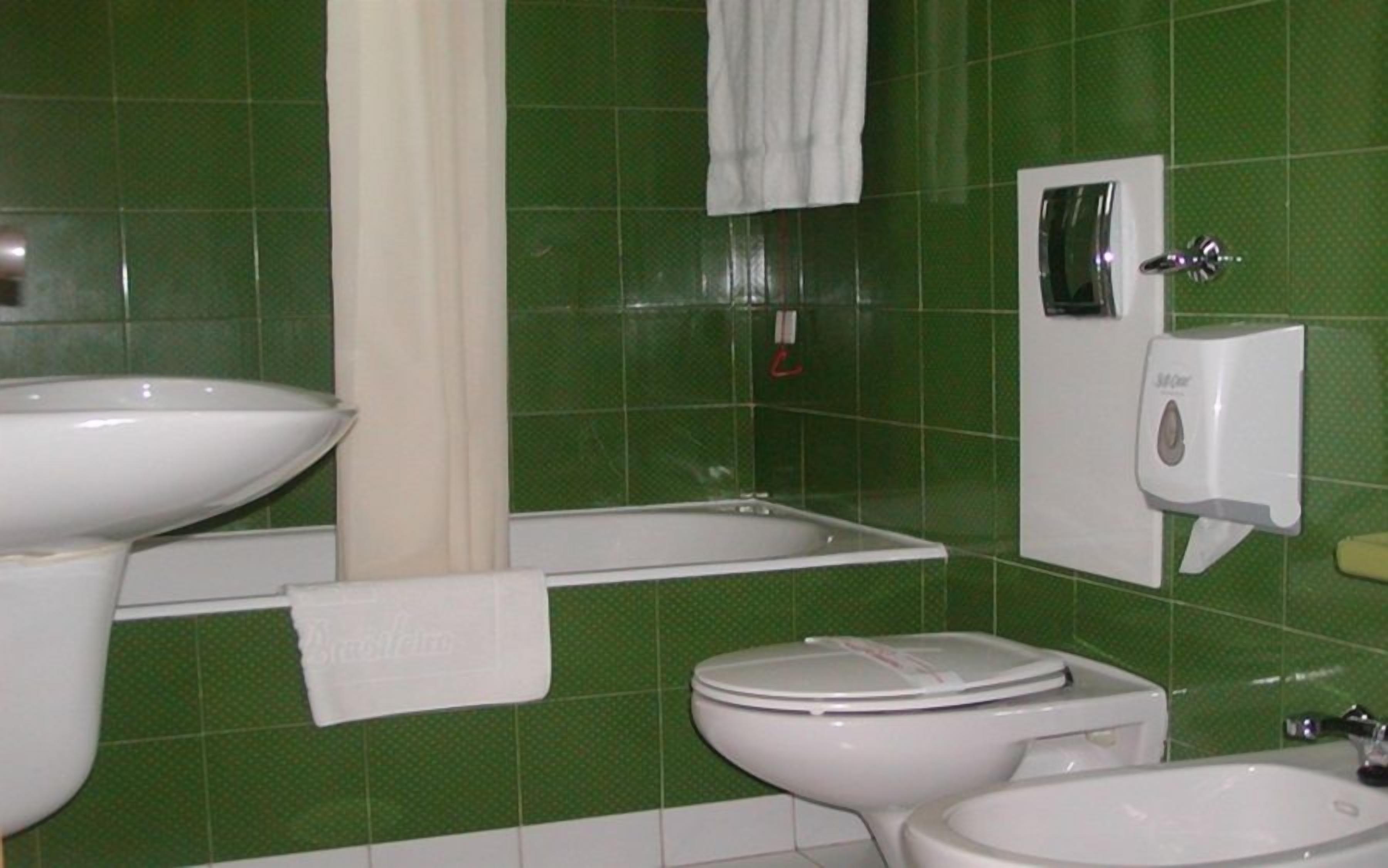 Un baño con paredes de azulejos verdes, un lavamanos blanco, una bañera, un inodoro y un secador de manos.