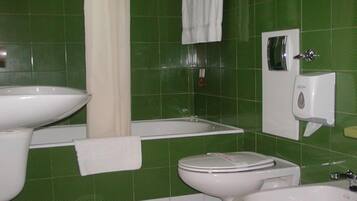 Un baño con paredes de azulejos verdes, un lavamanos blanco, una bañera, un inodoro y un secador de manos.