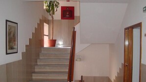 A staircase with a wooden handrail, a potted plant at the top, and a door to the right. - Luso Brasileiro (Povoa De Varzim)