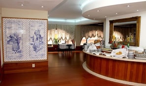 Een hotel lobby met een receptiebalie, een eetgedeelte en een decoratieve muur met kunstwerken.