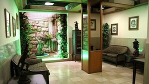 A room with a stone wall, a small fountain, and a statue. There are two chairs and a table. - Luso Brasileiro (Povoa De Varzim)