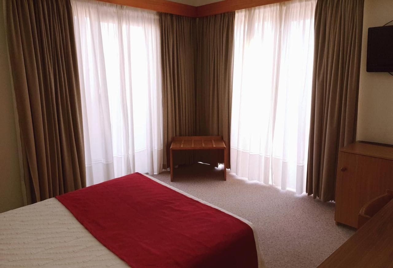 Una habitación de hotel con una cama, un banco de madera y un televisor en la pared.