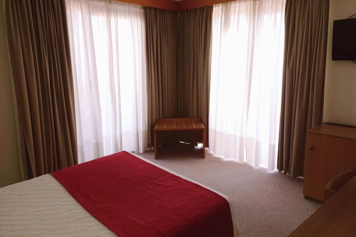Een hotelkamer met een bed, een houten bankje en een televisie aan de muur.