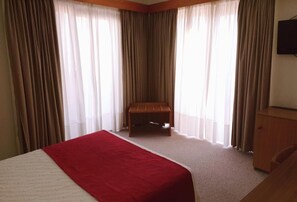 A hotel room with a bed, a wooden bench, and a TV on the wall. - Luso Brasileiro (Povoa De Varzim)