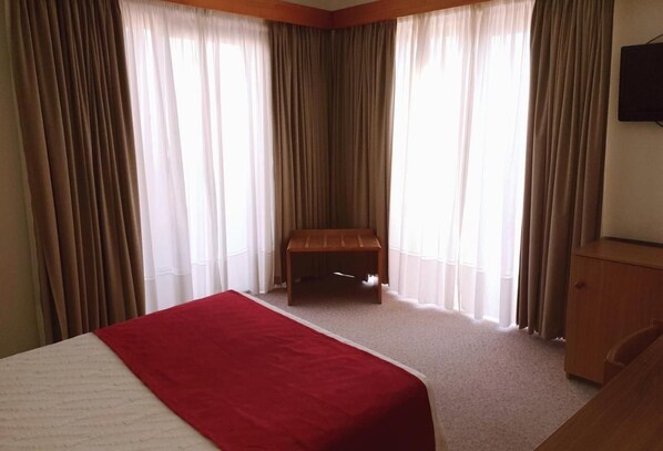A hotel room with a bed, a wooden bench, and a TV on the wall. - Luso Brasileiro (Povoa De Varzim)