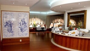 A hotel lobby with a reception desk, a dining area, and a decorative wall with artwork. - Luso Brasileiro (Povoa De Varzim)