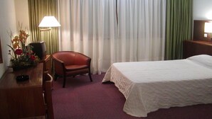 A hotel room with a bed, a desk, a chair, a lamp, and a window with curtains.