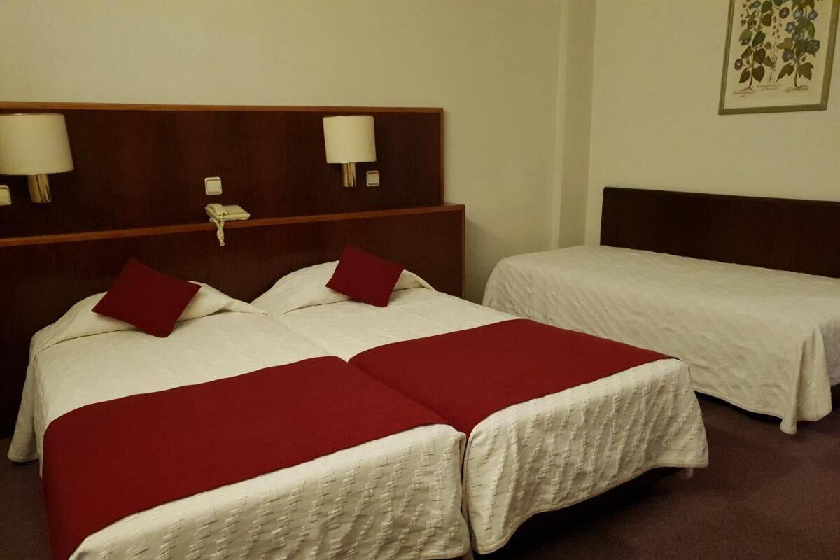 Habitación de hotel con dos camas, cada una con una colcha blanca y almohadas rojas, y cabeceros de madera con lámparas de pared.