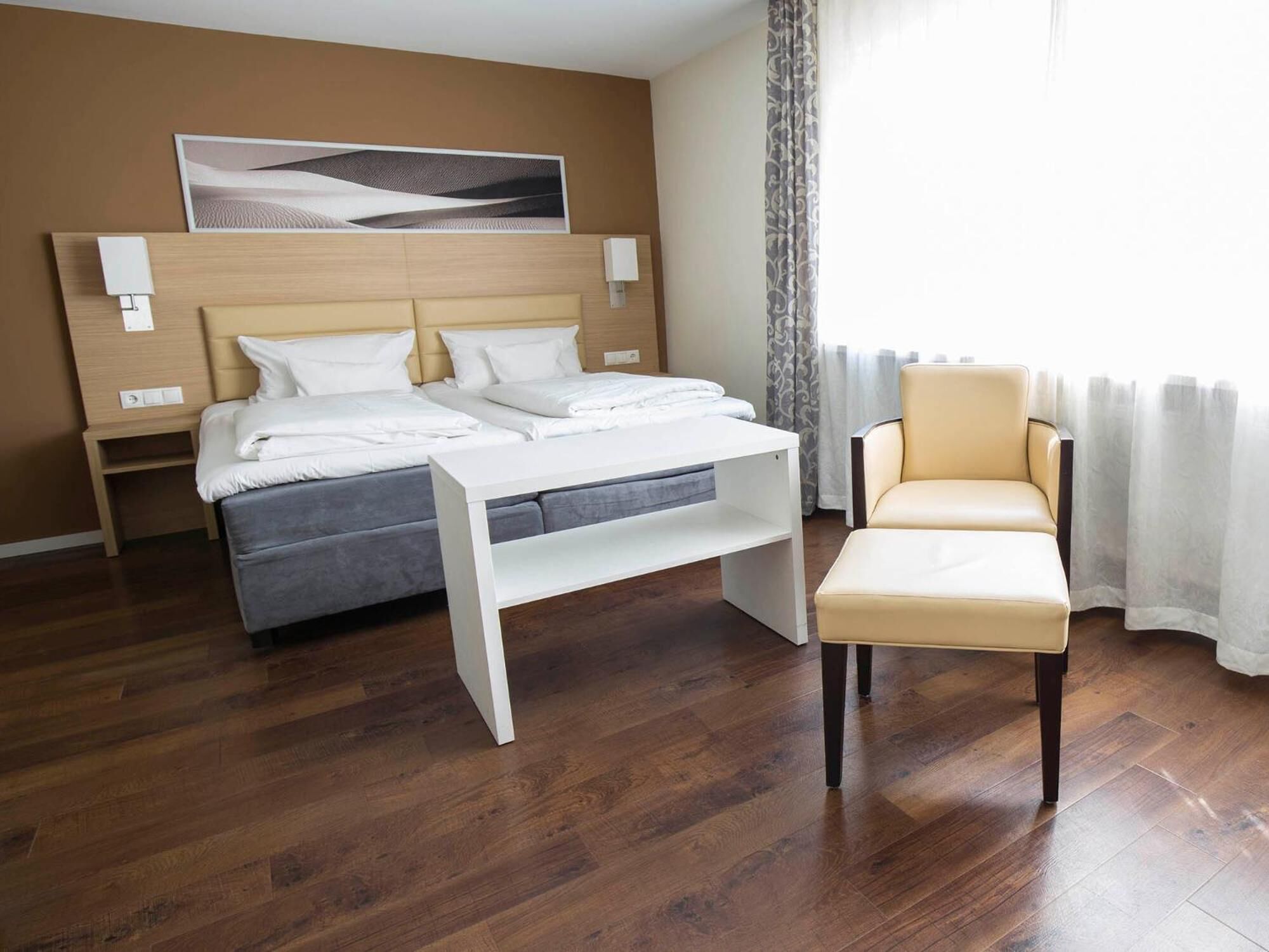 Une chambre d’hôtel avec un lit, une table de chevet, une chaise et une grande fenêtre avec des rideaux.